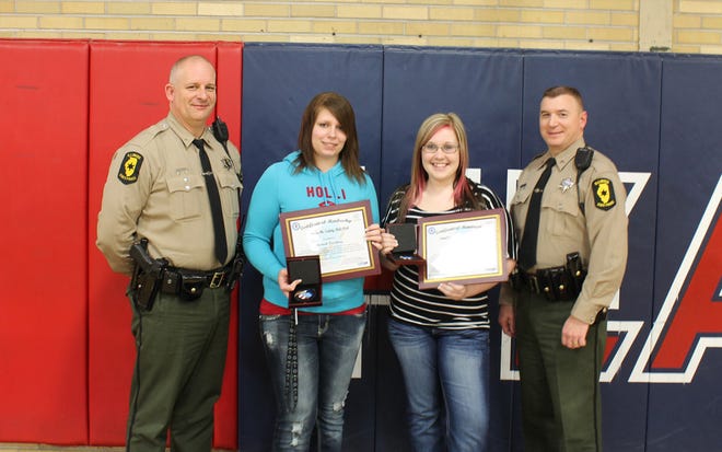 Illinois State Troopers Dan Hill and Brendan Schaley present medallions to Kaitlyn Lant and Hannah Woodbury last weekend at West Central High School.