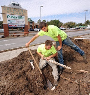 Grandview Landscaping employee Dakota Leffers, right, uses a shovel to take pressure off of a line so that fellow employee Joseph Leggett can removed the cut piece. The crew was working on removing old plants and tree stumps from the parking lot and surrounding area of Churchill Square Tuesday morning.