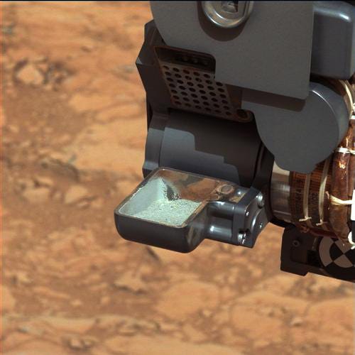 This image released by NASA shows the Curiosity rover holding a scoop of powdered rock on Mars. The rover recently drilled into a Martian rock for the first time and transferred a pinch of powder to its instruments to analyze the chemical makeup.