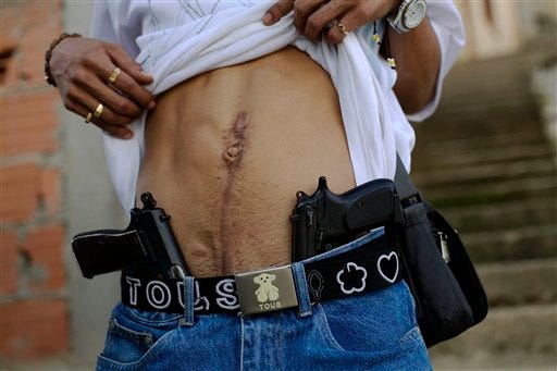 FILE - In this Nov. 25, 2007, drug dealer Joan, who identifies himself as "El Patan," shows his guns and a scar on his stomach from an injury suffered during clashes with rival gangs in Las Mayas neighborhood of Caracas, Venezuela. Violence has emerged as a top campaign issue as opposition Gov. Henrique Capriles challenges Chavez successor Nicolas Maduro in an April 14, 2013 election to replace the late leader, Hugo Chavez. (AP Photo/Rodrigo Abd, File)