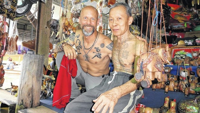A boat merchant shows David McGrain some of his wares as the two compare tatoos in a floating market area in Thailand. McGrain travels the world looking for members of dwindling native cultures that could use an infusion of cash to help maintain a heritage.