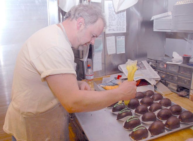 Owner Julius Richard Pfaff adds icing decoration to the chocolate egg cakes, which are basically white pieces of egg-shaped cake covered in chocolate frosting with different frosting colors on top.