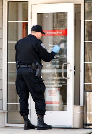 An officer from the Plymouth County Bureau of Criminal Investigation dusts for fingerprints on the door of the Sovereign Bank branch on Plain Street in Marshfield after it was robbed on Monday, April 1, 2013.
