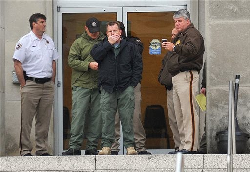 Law enforcement officers wait at the entrance to the Jackson Police Department Thursday, April, 4, 2013, after police say a murder suspect fatally shot detective Eric Smith inside the headquarters. The suspect is also dead.