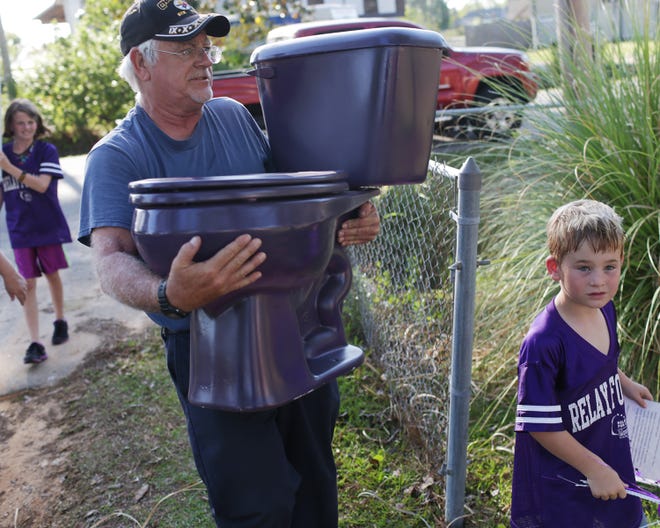 Donal Ross carries a purple toilet into the yard of former Callaway Mayor Ken Meer as part of a fundraiser for the American Cancer Society on Wednesday. Also in the photo are Faith Ross, left, and Danni Currington.