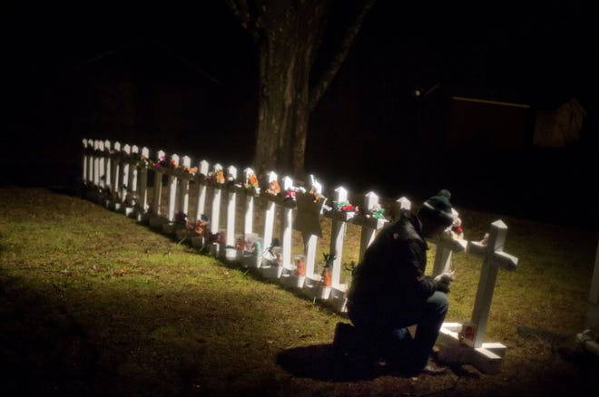 Frank Kulick adjusts a display of wooden crosses, and a Jewish Star of David, representing the victims of the Sandy Hook Elementary School shooting, on his front lawn, in Newtown, Conn.