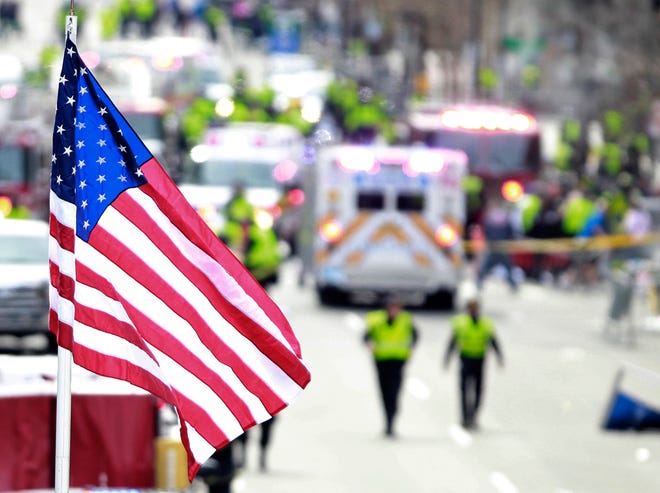 A flag flies over the finish line as medical workers aid injured people following an explosion at the finish line of the 2013 Boston Marathon in Boston, Monday, April 15, 2013. Two explosions shattered the euphoria at the finish line, sending authorities out on the course to carry off the injured while the stragglers were rerouted away from the smoking site of the blasts. (AP Photo/Charles Krupa)