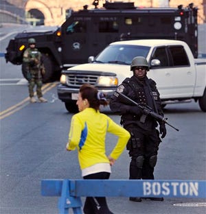 A runner passes a police officer dressed in tactical gear, who blocks a road leading to the Boston Marathon route, the morning after explosions killed three and injured more than 140 in Boston, Tuesday, April 16, 2013. The bombs that blew up seconds apart at the finish line of one of the world's most storied races left the streets spattered with blood and glass, and gaping questions of who chose to attack at the Boston Marathon and why.