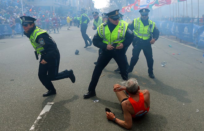 Bill Iffrig, 78, lies on the ground as police officers react to a second explosion at the finish line of the Boston Marathon in Boston, Monday, April 15, 2013. Iffrig, of Lake Stevens, Wash., was running his third Boston Marathon and near the finish line when he was knocked down by one of two bomb blasts.