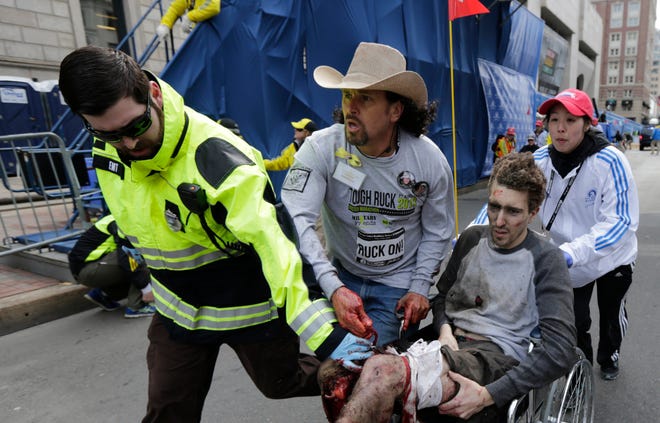 An emergency responder and volunteers, including Carlos Arredondo in the cowboy hat, push Jeff Bauman in a wheel chair after he was injured in an explosion near the finish line of the Boston Marathon Monday, April 15, 2013 in Boston. At least three people were killed, including an 8-year-old boy, and more than 170 were wounded when two bombs blew up seconds apart. (AP Photo/Charles Krupa)