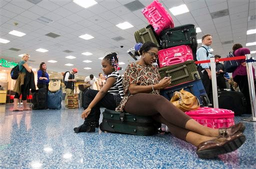 Daija Walker, left, and Andrea Clarke sit next to their luggage at the Miami International Airport, Tuesday in Miami, as they tried to get back home to Barbados. A computer system used to run many daily operations at American Airlines failed Tuesday, forcing the nation's third-largest carrier to ground all flights across the United States for several hours and stranding thousands of frustrated passengers at airports and on planes.