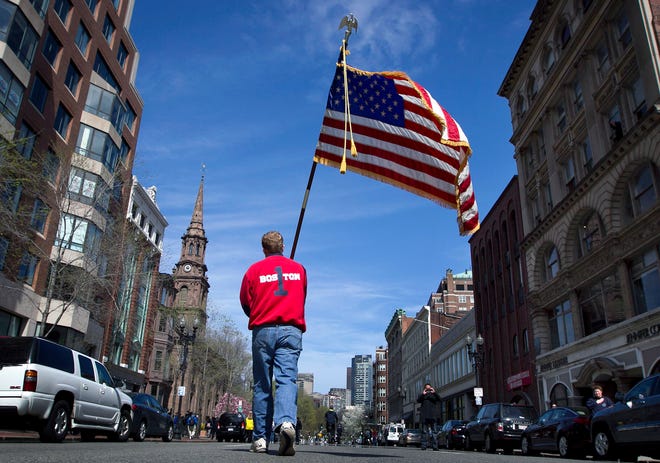 Lt. Mike Murphy of the Newton, Mass., fire dept., carries an American flag down the middle of Boylston Street after observing a moment of silence in honor of the victims of the bombing at the Boston Marathon near the race finish line, Monday, April 22, 2013, in Boston, Mass. At 2:50 p.m., exactly one week after the bombings, many bowed their heads and cried at the makeshift memorial on Boylston Street, three blocks from the site of the explosions, where bouquets of flowers, handwritten messages, and used running shoes were piled on the sidewalk. (AP Photo/Robert F. Bukaty)
