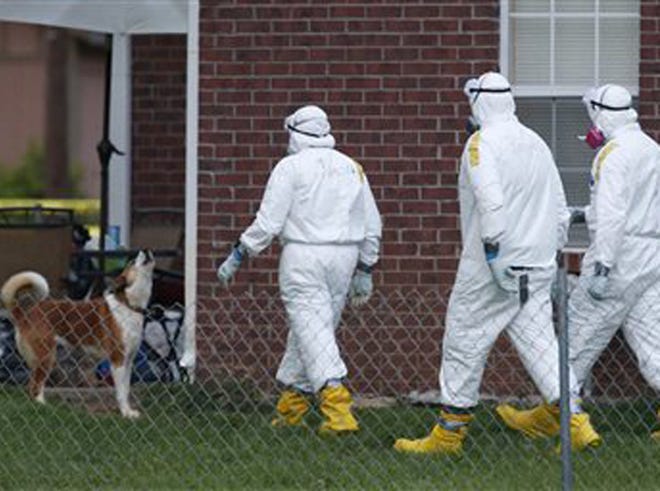 Federal agents wearing hazmat suits inspect the grounds around the house owned by Everett Dutschke, in connection with the recent ricin attacks, as one of his dogs howls Tuesday, April 23, 2013 in Tupelo, Miss. No charges have been filed against Dutschke and he hasn’t been arrested.