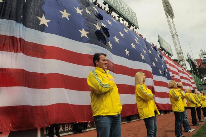 Marathon volunteers stand in front of the American flag draped over the Green Monster during Saturday's pre-game ceremony honoring the victims, first responders and others involved in the attacks on the 2013 Boston Marathon.