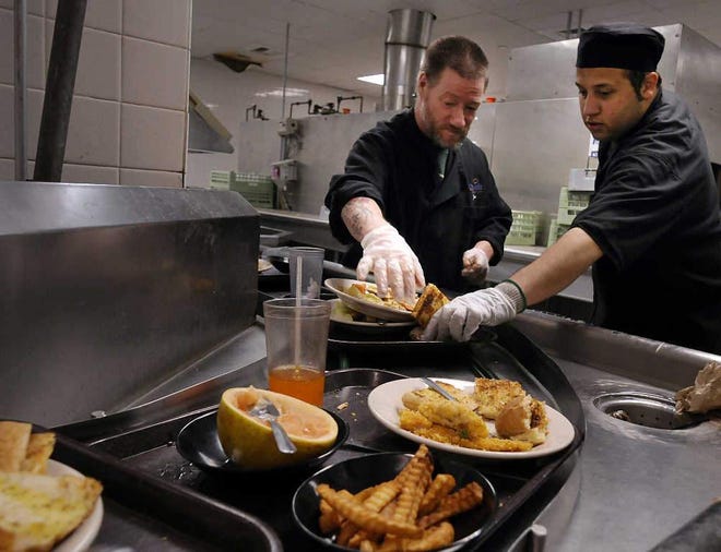 Cafeteria workers David Taylor, left, and Jaydden Burgos clear uneaten food from trays coming in to be cleaned in Fitchburg State University';s dining hall on Thursday.