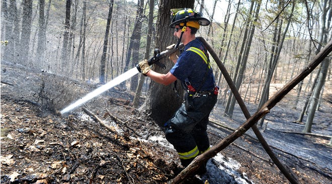 Wayland Firefighter Dean Casali blasts water into smoldering peat on the forest floor. Wayland firefighters spent the better part of Monday morning and early afternoon fighting a persistent 3-acre brush fire along the MWRA aqueduct off of Stonebridge Road. Changing wind, difficult terrain and thick peat hampered efforts to get the fire quickly under control.