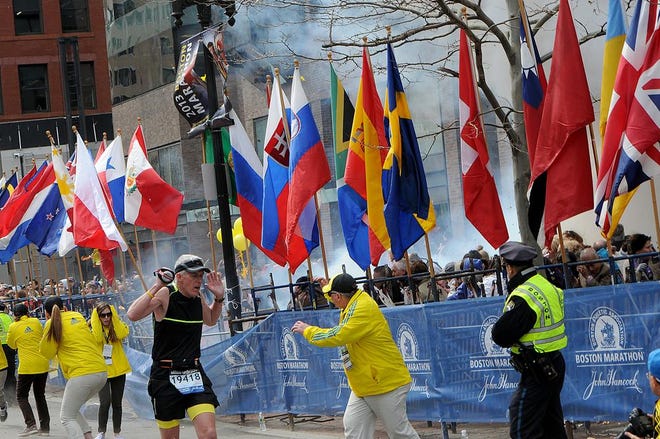 Runners, marathon officials and police react as an explosion goes off at the Boston Marathon finish.