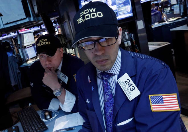 Specialists Devin Cryan, left, and Gabriel Freytes wear a "Dow 15,000" hats as they work at a post on the floor of the New York Stock Exchange.