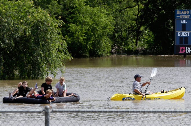 A kayaker pulls a raft with children around a flooded baseball park in San Antonio.