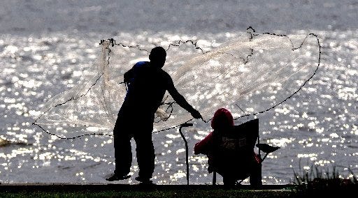 A fisherman throws a cast net off the seawall along the St. Johns River at the end of Post Street.