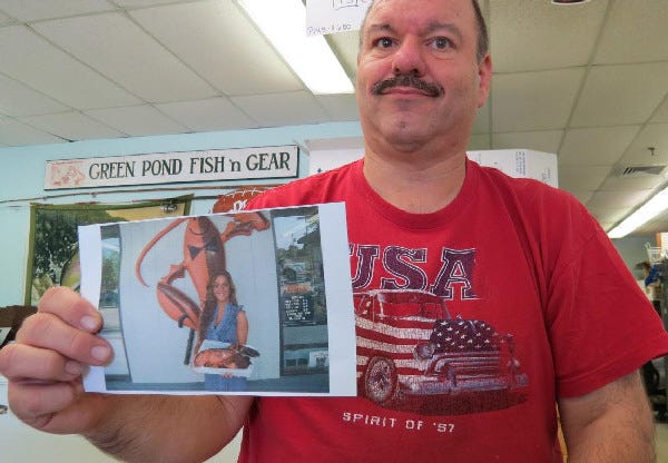 Bob Lewis, owner of the Green Point Fish Market in East Falmouth, holds a photo showing Rocky, the 5-foot-tall fiberglass lobster that until recently graced the front of his business. Lewis has offered a $100 reward for its safe return.