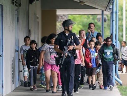 A Santa Monica police officer leads children on a field trip from Citizens of the World Charter School in Los Angeles out of Santa Monica College, where they had gone for a planetarium show, following a shooting in the area, in Santa Monica, Calif., Friday, June 7, 2013. Two people were found dead Friday in a burned home near the campus, where someone sprayed a street corner with gunfire. (AP Photo/Reed Saxon)