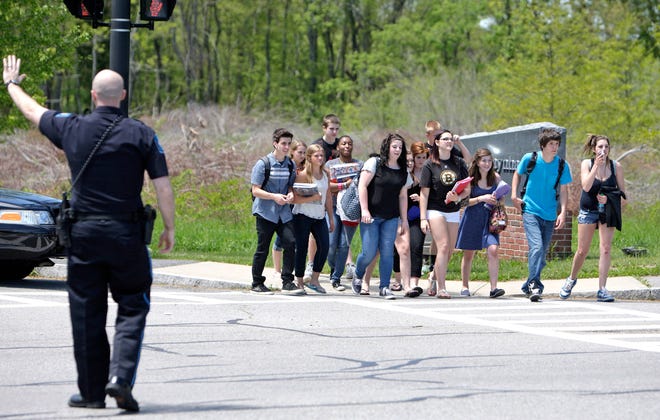 Bridgewater State University officer Thomas Mori stops traffic for students leaving Bridgewater-Raynham Regional High School after early dismissal follwing a reported bomb threat on Thursday.