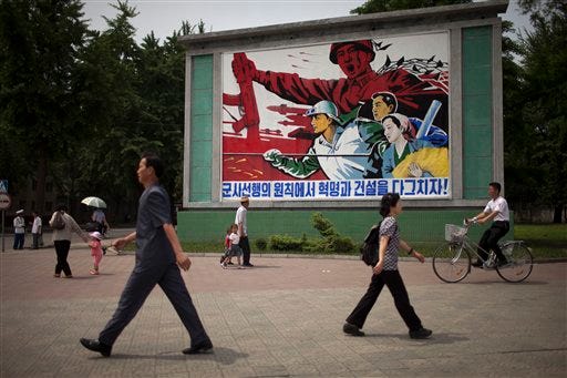 People walk past a roadside propaganda billboard promoting the "military first" policy and a boost to build the country's economy in Pyongyang, North Korea, Sunday, June 16, 2013. North Korea's top governing body on Sunday proposed high-level nuclear and security talks with the United States in an appeal sent just days after calling off talks with rival South Korea. (AP Photo/Alexander Yuan)