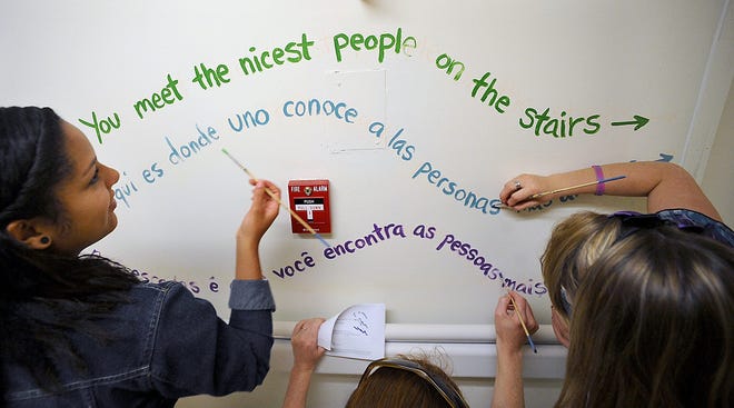 Blackstone Valley Tech painting and design students Vitoria Marcal, left, and Sarah Gover, and community mural artist Tova Speter of Newton, center, paint a quotation in three languages outside a stairwell at Milford Regional Medical Center Tuesday.