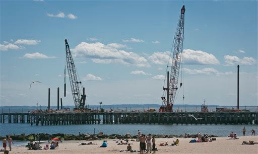 This June 12, 2013 photo shows cranes repairing a pier that was damaged during superstorm Sandy while visitors take to the beach in the Coney Island neighborhood in the Brooklyn borough of New York. (AP Photo/Bebeto Matthews)