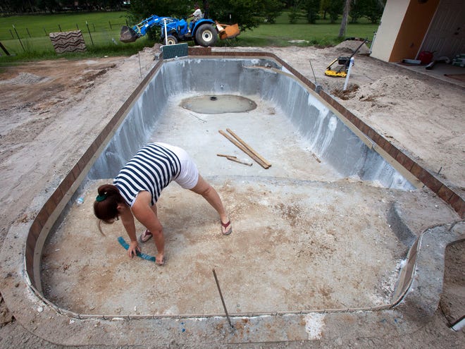 Customer Joanne Neal places some accent pieces of glass tile to get an idea what design she might like as pool contractor Mike Folsom and his employee Barry Jordan work on back-filling the 14-foot by 34-foot pool on North Magnolia in Anthony on Tuesday.