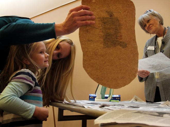 After Museum Educator Mary Moore, right, ironed the piece, Ashlyn Hallick, 4, smiles as her mother, Lindy, holds up her version of cave art at the Appleton Museum of Art in Ocala.