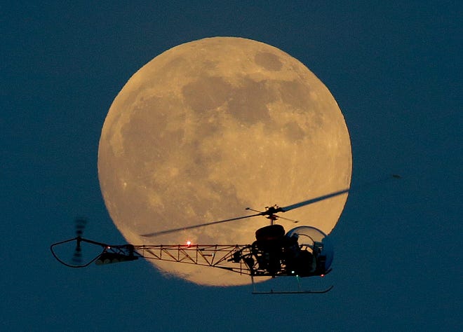 The moon is seen in its waxing gibbous stage as it rises Saturday night behind the helicopter from the original "Batman" television show, which people can ride at the New Jersey State Fair in East Rutherford, N.J. The moon, which reached its full stage early Sunday, is expected to be 13.5 percent closer to earth during a phenomenon known as supermoon.