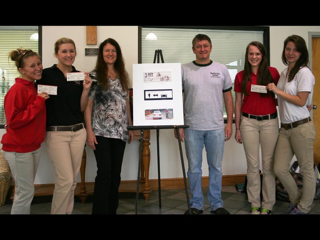 From left are Holy Spirit Catholic School students Lizzy Boyles and Taylor Elmore, teacher Tricia Schuster, Queen City Cycles co-owner Jason Capley, and students Sarah Walmsley and Savannah Barder. Above is Boyles’ design, which earned first prize. Elmore’s earned second prize and Walmsley and Barder’s earned third prize.