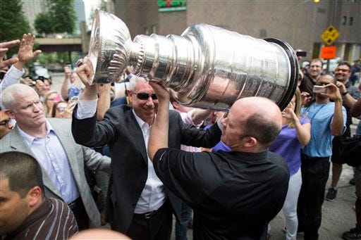 Chicago Blackhawks NHL hockey president and CEO John McDonough, center facing, hoists the Stanley Cup Trophy outside a Chicago steakhouse, Tuesday, June 25, 2013. McDonough was joined by Blackhawks owner Rocky Wirtz at the restaurant.