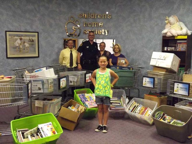 Sweetwater Elementary School student Grace Agostinis, 8, stands among the more than 2,000 books she collected for the Children’s Home Society. Behind her are (from left) Assistant Principal Adrian Bronson, Grace’s parents Michael and Gail Agostinis, and Children’s Home Society Director Shirley Jeter.