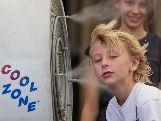 Ten-year-old Easton Martin, of Mesa, Ariz., stops to cool off in a misting fan while walking along The Strip with his family in Las Vegas. A blazing heat wave expected to send the mercury soaring to nearly 120 degrees in Phoenix and Las Vegas settled over the West on Friday, threatening to ground airliners and raising fears that people and pets will get burned on the scalding pavement.