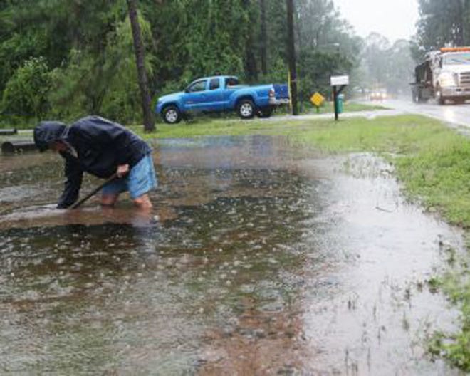 Gary Bryant attempts to unclog a drain from the bottom of a ditch to help with flooding on his property during a downpour in Panama City Beach on Thursday.