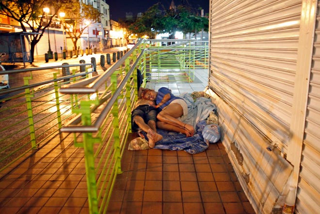 In this June 26, 2013 photo, a homeless couple sleeps in front of a closed business in San Juan, Puerto Rico. Nearly 80 percent of previous cases involving homeless people were tied to drugs, but that financial and family problems now play a bigger part. "We're seeing more women on the street," said the Puerto Rico Pro Homeless Coalition of Coalitions' executive director. (AP Photo/Ricardo Arduengo)