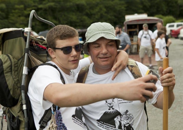 Boy Scout Brendan Rearick, 15, of Hookstown uses a smart phone to snap a picture with his father and hike leader Bill Rearick before the start of Troop 496's 25th annual 100-mile hike outside of Mill Creek Presbyterian Church. The hikers left Mill Creek Sunday afternoon and will arrive at Camp Heritage Reservation in Farmington on Saturday, covering 10 to 22 miles a day. Forty-four people, including current Boy Scouts and former Scouts who previously did the hike were participating. While some were hiking the whole 100 miles, others were doing smaller sections.