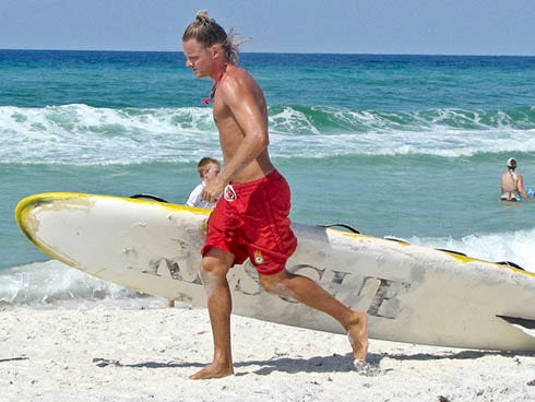 South Walton Fire District lifeguard Brad Stewart carries a surfboard to the water recently. The guards spend their days manning watch towers and advising beachgoers about water safety.