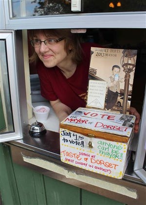 In this photo made Wednesday, June 26, 2013 in Dorset , Minn., Jeannette Dudley, co-owner of Dorset House Family Restaurant, poses by the ballot box at the window of her restaurant in the Dorset mayor race. Bobby Tufts, the 4-year-old mayor, is running for re-election. Bobby was only 3 when he won election last year as mayor of Dorset (population 22 to 28, depending on whether the minister and his family are in town). Dorset, which bills itself as the Restaurant Capital of the World, has no formal city government. (AP Photo/Jeff Baenen)