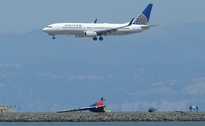 The tail of Asiana Flight 214 is sits on the tarmac as a United Airlines plane lands at San Francisco International Airport in San Francisco, Monday, July 8, 2013. An Asiana Airlines Boeing 777 crashed upon landing Saturday, July 6, at San Francisco International Airport, and two of the 307 passengers aboard were killed. Investigators said Asiana Airlines Flight 214 was traveling "significantly below" the target speed during its approach and that the crew tried to abort the landing just before it smashed onto the runway. (AP Photo/Jeff Chiu)