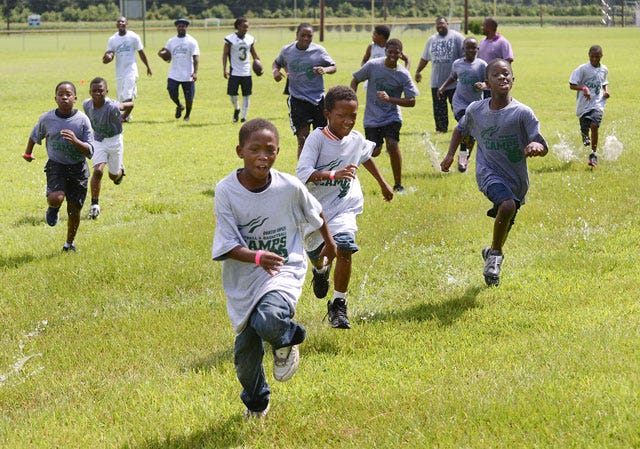 Football campers sprint across a rain-soaked field at Kinston High School during Quinton Coples’ football camp Saturday at Kinston High School.