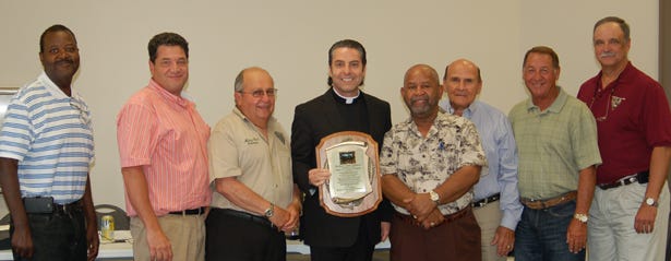Father Cleo Milano, who served as pastor of St. John the Evangelist Catholic Church in Plaquemine for 11 years, was honored by Mayor "Tony" Gulotta and the Plaquemine Board of Selectmen at its June 25 meeting. The officials praised him for his dedication to the community, inspiration, and willingness to work with residents of all religions, along with his contribution to beautifying downtown Plaquemine with the addition of the plaza and beautiful lighted fountain at the front of the church. He is shown accepting a plaque presented to him at the meeting. Shown from left are, Selectman Jimmie Randle, Jr., Mayor Gulotta, Selectman Mickey Rivet, Father Cleo, and Selectmen Oscar Mellion, Ralph Stassi, Jr., Lin Rivet, Jr., and Timmy Martinez.