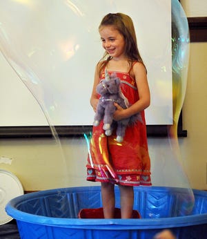 Chloe Gareau, 4, of Grafton, holds on to her unicorn stuffed animal as she is encased in a large bubble during Mike the Bubble Man's (Mike Dorval of Ashland) program at the Franklin Public Library Wednesday.