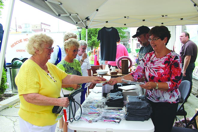 Hot off the press, Greencastle-Antrim Old Home Week badges flew off the table during Sidewalk Days Friday and Saturday in Greencastle. In addition to the badges, Tom Stine and Linda Reed (right) sold T-shirts and hats. Nancy Taylor and Connie Fennen (left) were pleased to add badges for the Aug. 3 to 10 celebration to their shopping bags during the downtown event.