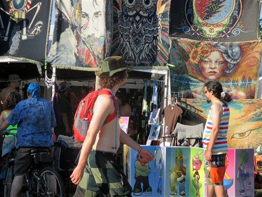 In this Friday, July 26 photo released by Paul Duning, a music fan at the Gathering of the Vibes festival walks by a vendor selling souvenirs including one with the image of the late Jerry Garcia, the Grateful Dead guitarist who died in 1995. The festival draws about 20,000 fans to this small city on the Connecticut coast and features a wide variety of bands including offshoots of the Grateful Dead.