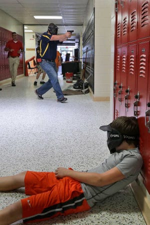 In this photo taken July 11, 2013, a Clarksville schools faculty member, wearing a protective mask, rear center, carries a practice handgun toward a classroom in the city's high school in Clarksville, Ark., as students portray victims in a mock school shooting scenario. Twenty Clarksville School District staff members are training to be armed security guards on campus. (AP Photo/Danny Johnston)