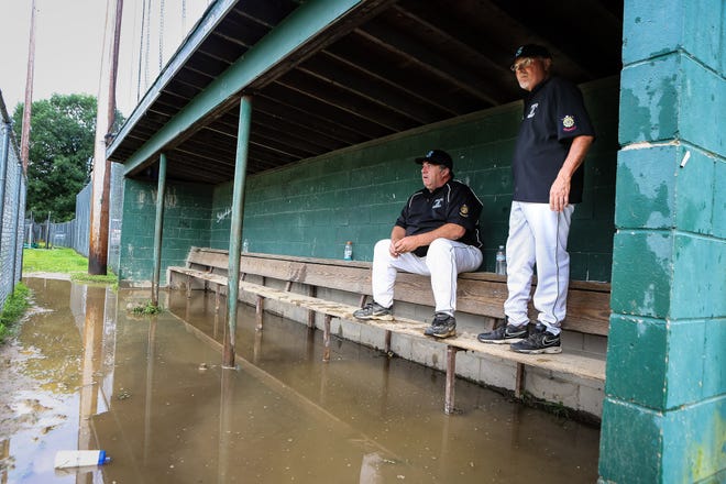 Sudbury Post 191 manager Len Noce (left) and assistant coach Eric Natoli sit in a flooded dugout after Sudbury's American Legion playoff game against Medford Post 45 was postponded Monday evening.